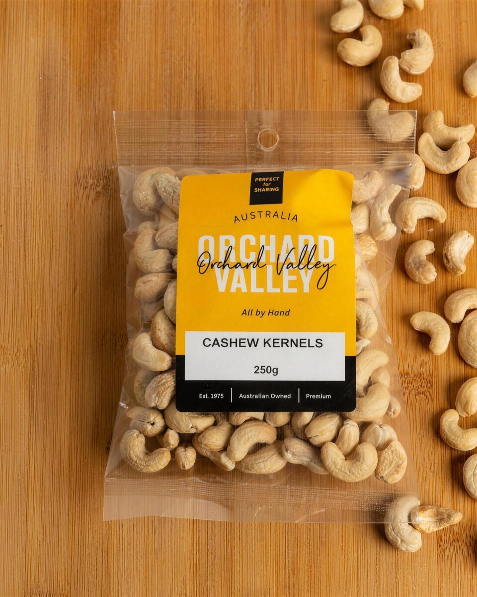 Orchard Valley Cashew Kernels 250g on a timber board with loose cashews.
